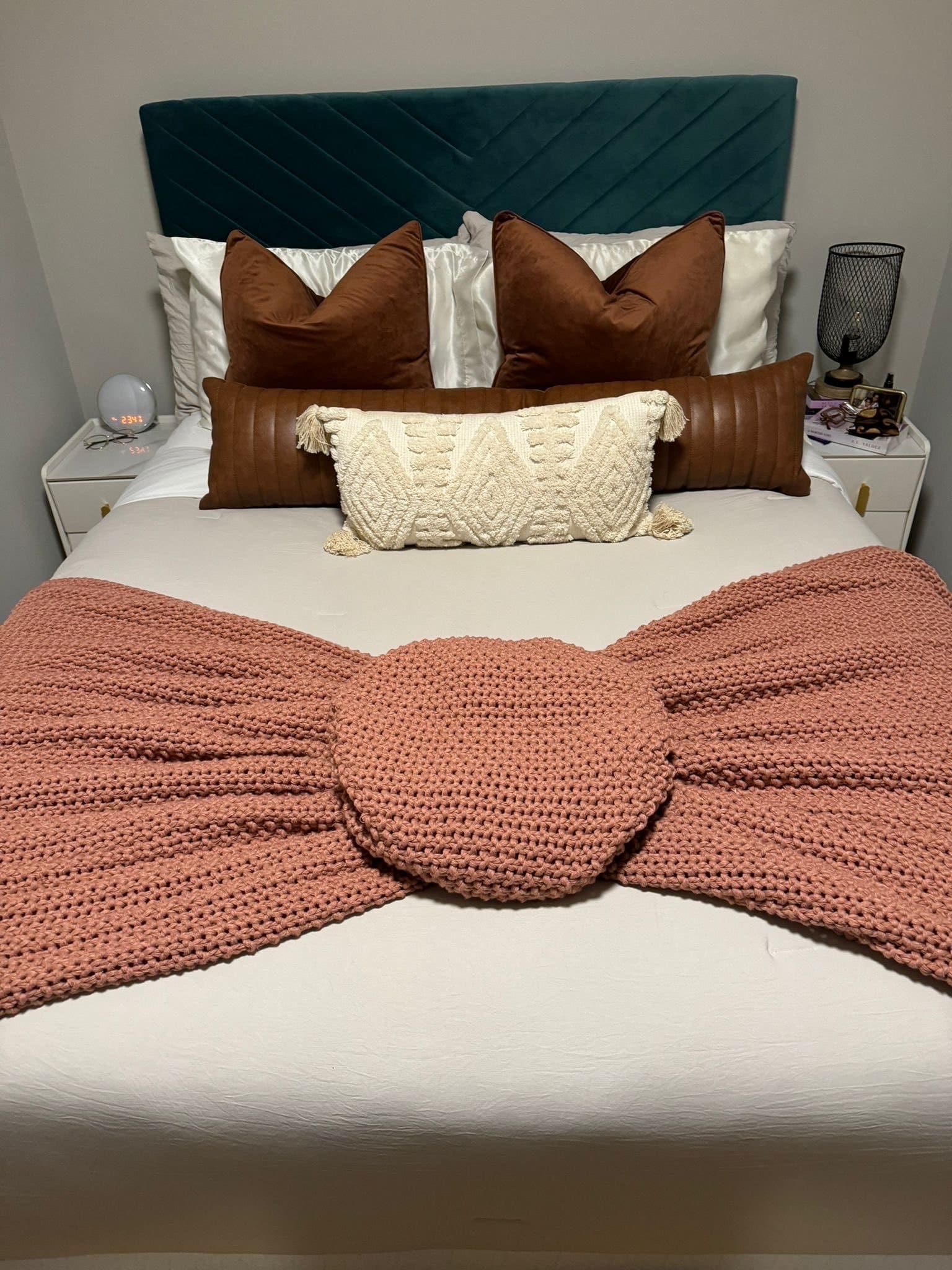 Made bed with velvet and leather pillows and a pink knit throw tied into a bow