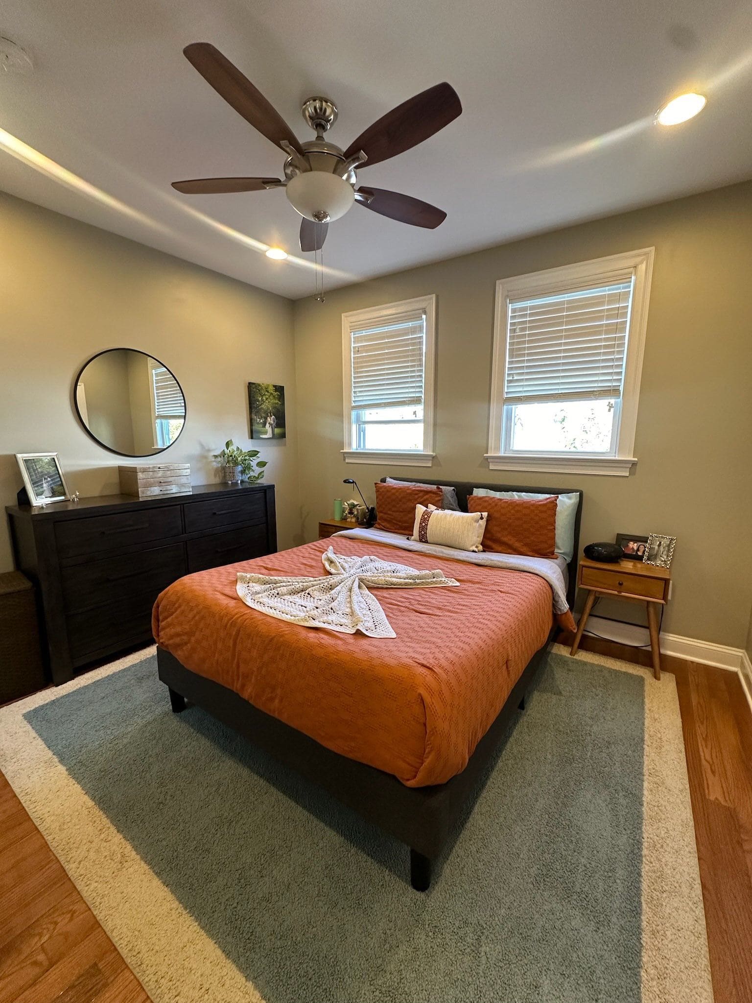 Bedroom with orange bedding, a folded towel on the bed and a ceiling fan