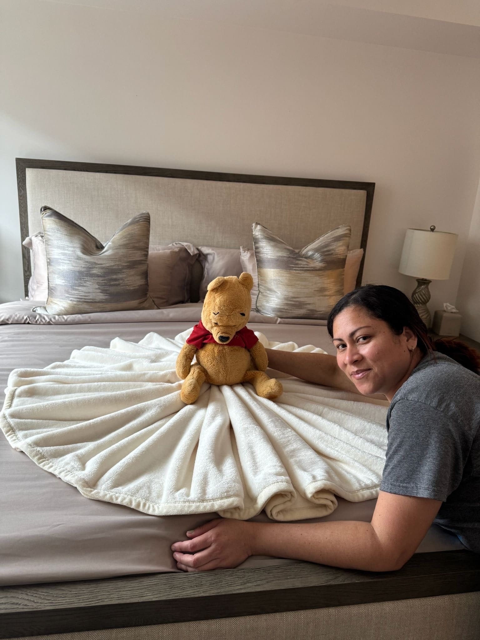 A Bradshaw team member beside a freshly made bed with a Winnie the Pooh plush and a fanned white towel