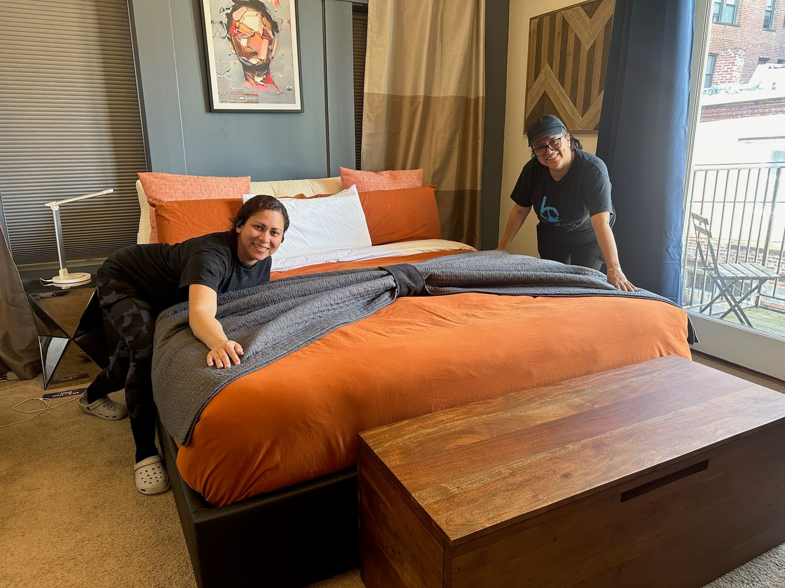 Two Bradshaw Cleaning team members smiling as they finish making a bed with orange bedding