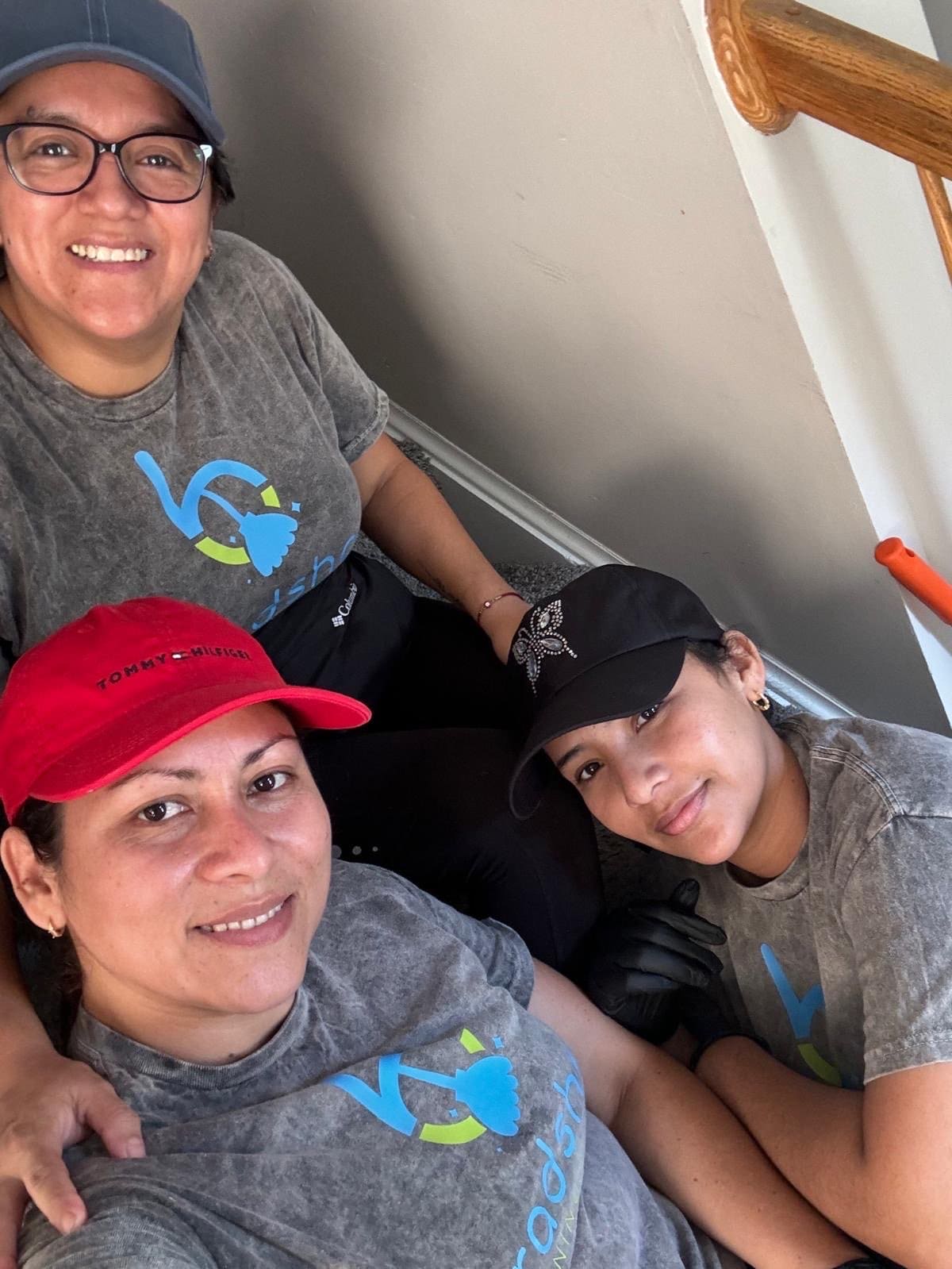 Three Bradshaw Cleaning team members in branded shirts and caps taking a selfie on a staircase